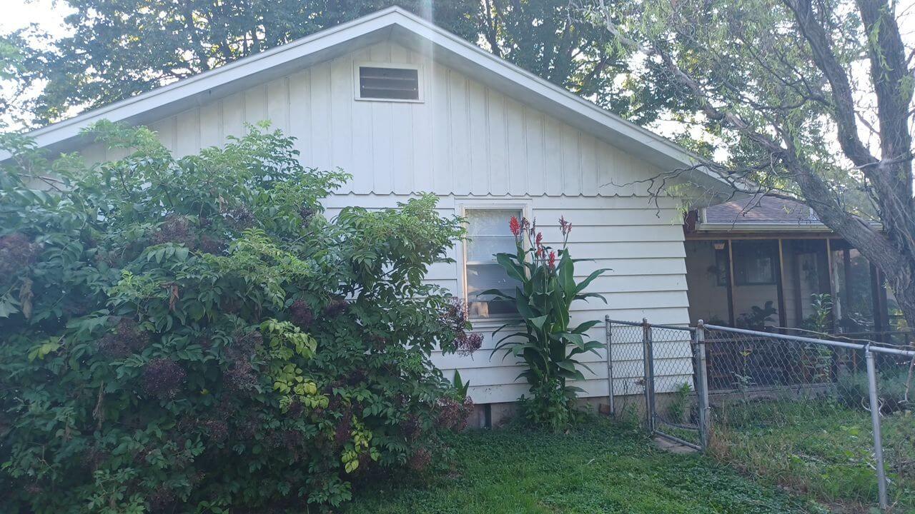 White vinyl siding house exterior with overgrown bushes in Lawrence, KS
