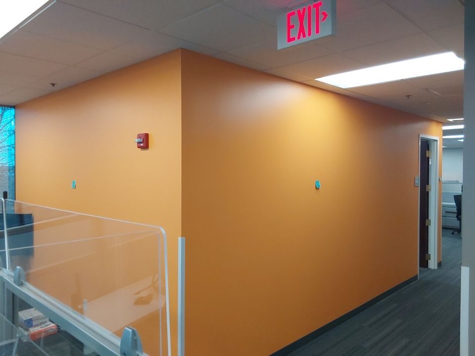 Orange painted office hallway with exit sign and fire alarm.