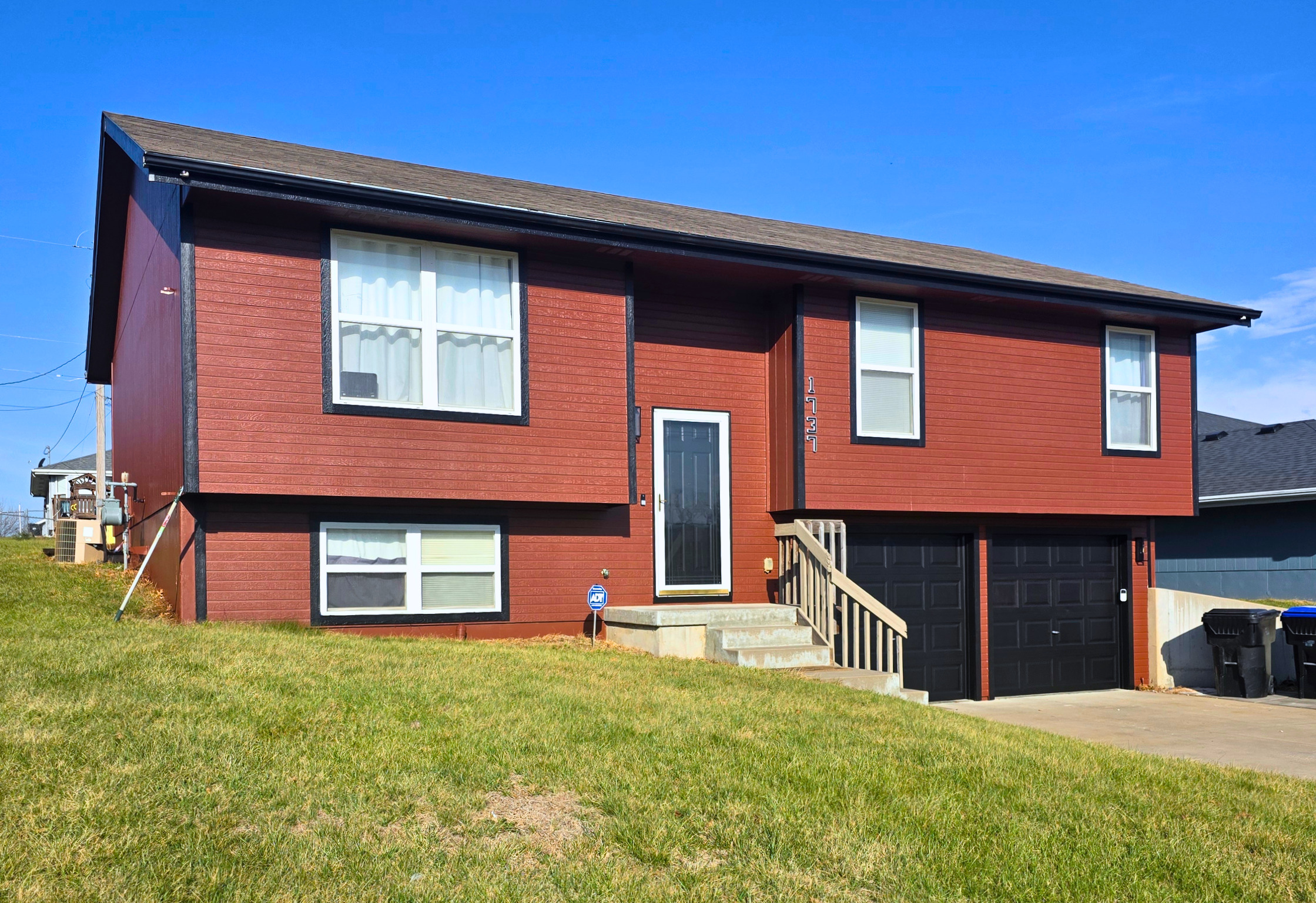 Red split-level home with attached two-car garage and lush green lawn.
