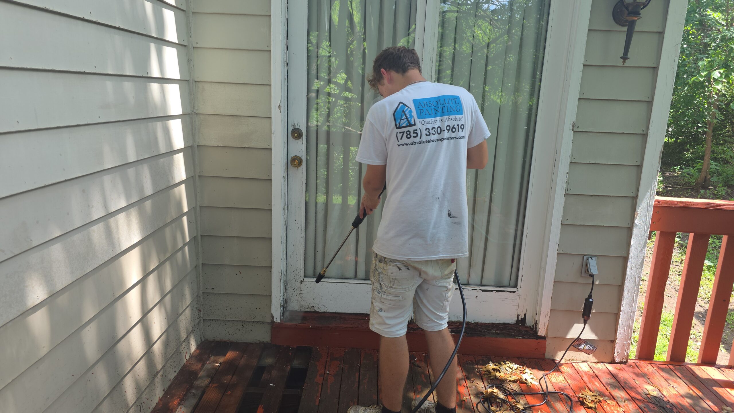 Topeka pressure washing technician cleans a wooden deck and siding.